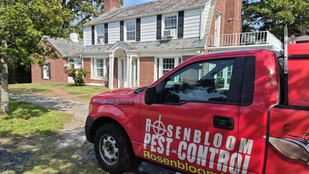 Rosenbloom Pest Control truck parked in the driveway of a brick and white colonial-style home